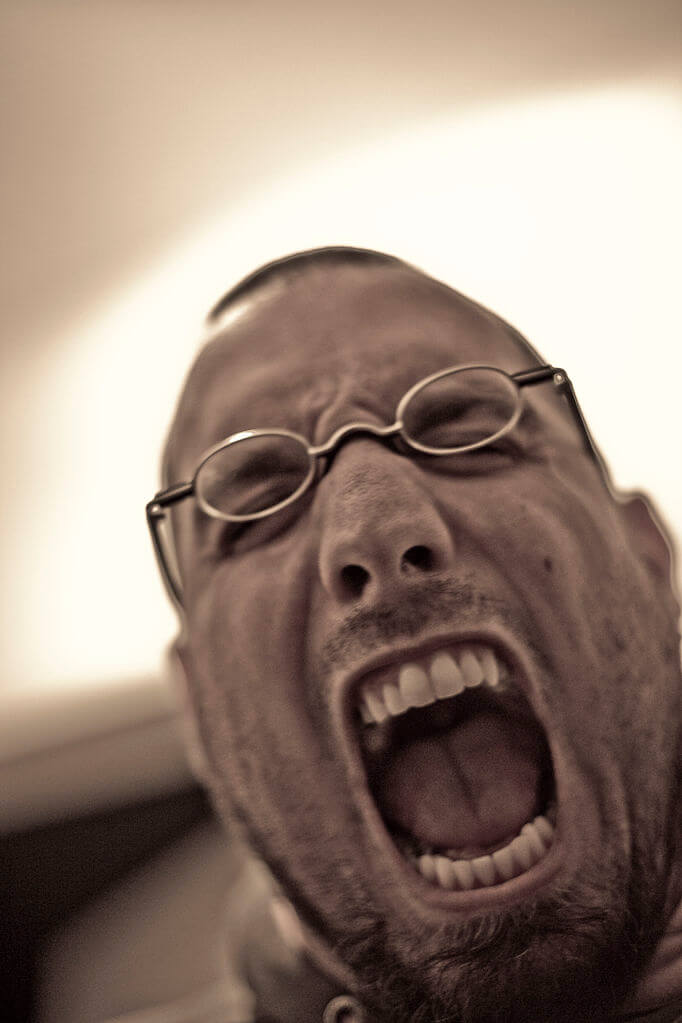 Man's face screaming/shouting. Stubbly wearing glasses. Credit https://commons.wikimedia.org/wiki/File:Scream_crosathorian.jpg