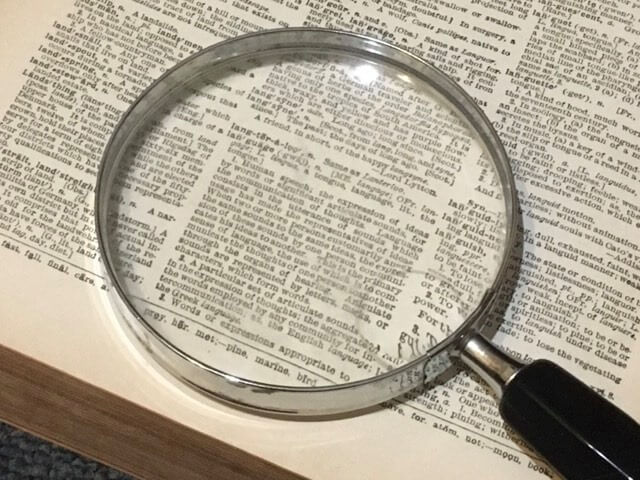 Magnifying glass on the page of a book. Credit: https://commons.wikimedia.org/wiki/File:Magnifying_glass_on_the_page_of_a_book.jpg